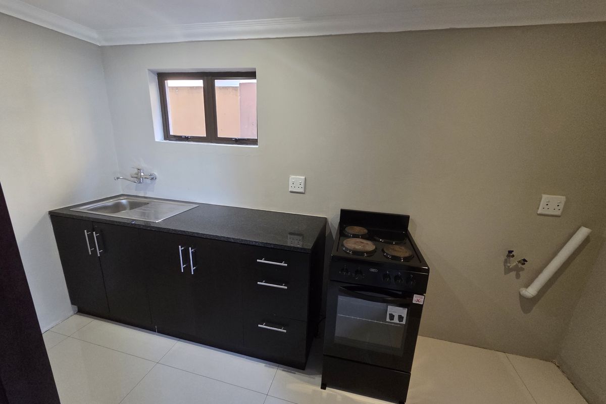 A clean, functional kitchen featuring dark cabinetry, granite countertops, a stainless steel sink, and a freestanding stove with tiled flooring.
