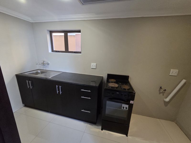 A clean, functional kitchen featuring dark cabinetry, granite countertops, a stainless steel sink, and a freestanding stove with tiled flooring.