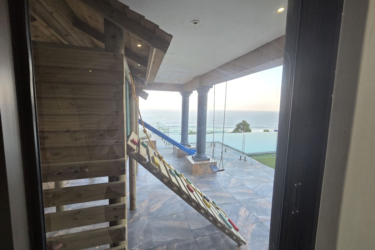 Spacious covered patio featuring high-end tiled flooring, stone columns, and a glass balustrade overlooking an infinity pool with ocean views.
