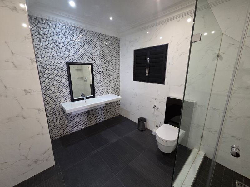 Modern bathroom featuring a wall-mounted vanity, mosaic tile accent wall, marble-look wall tiles, glass shower enclosure, and a wall-hung toilet.