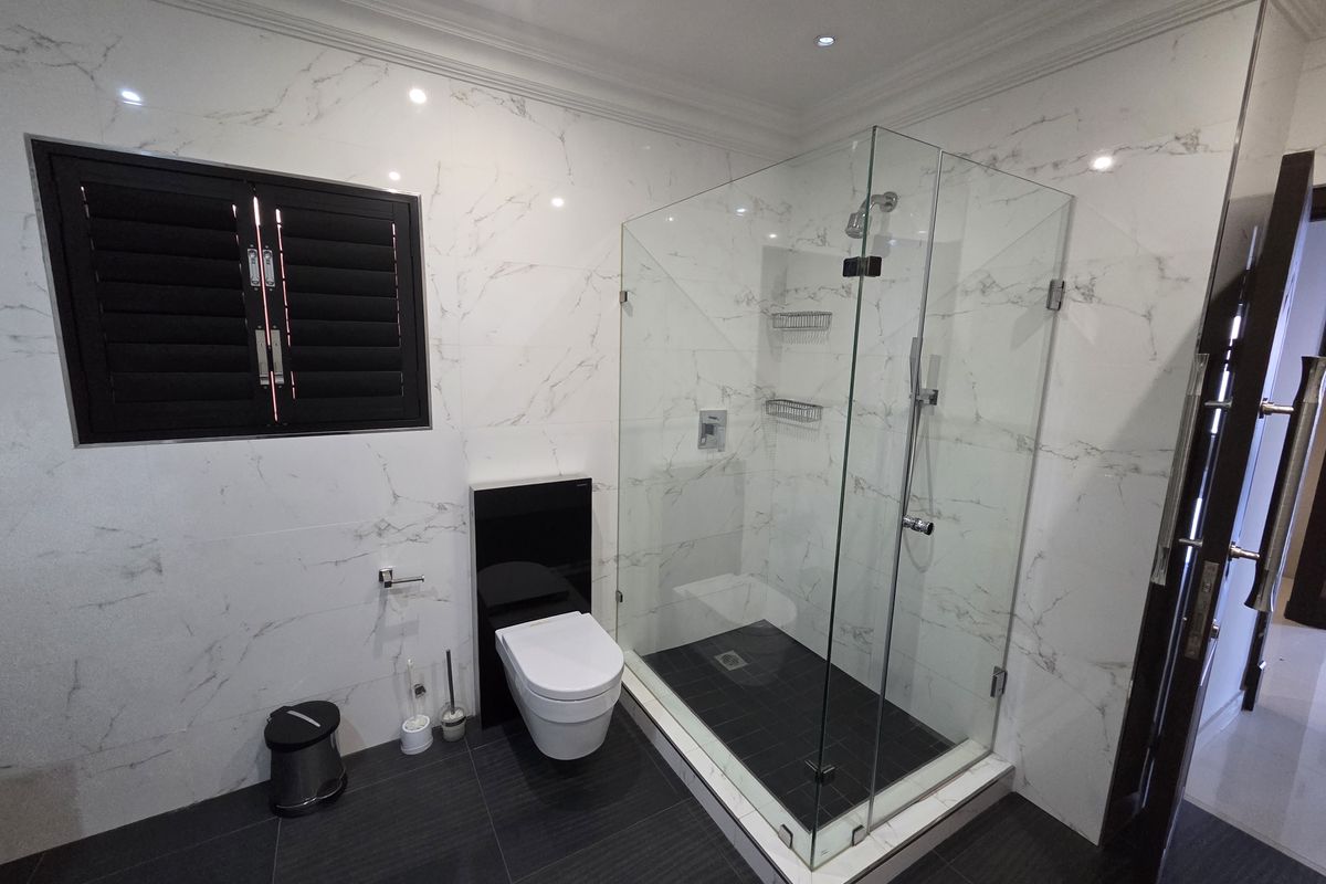 Modern bathroom featuring a glass-enclosed shower, wall-mounted toilet, and elegant marble-look wall tiling with contrasting dark floor tiles.