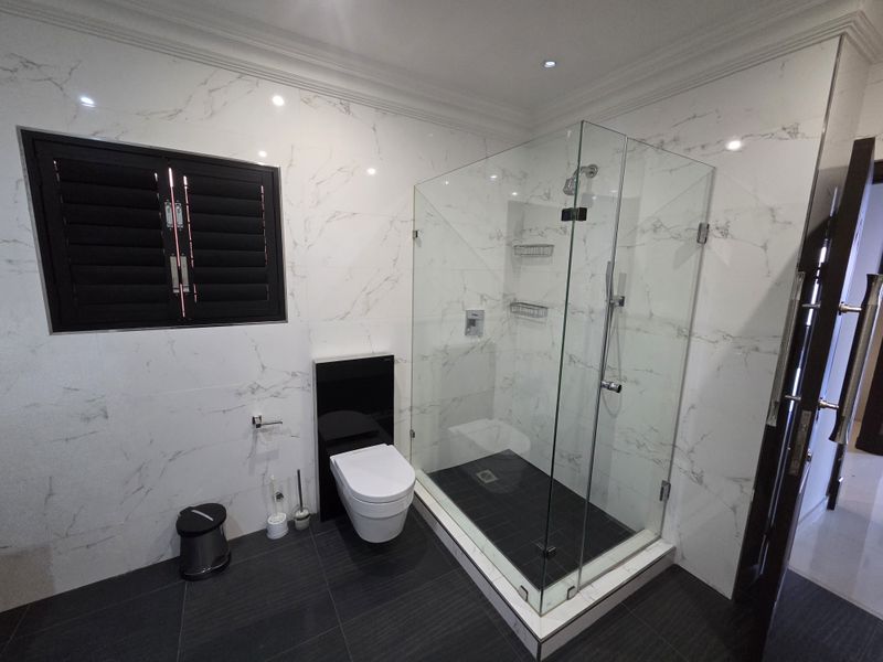 Modern bathroom featuring a glass-enclosed shower, wall-mounted toilet, and elegant marble-look wall tiling with contrasting dark floor tiles.