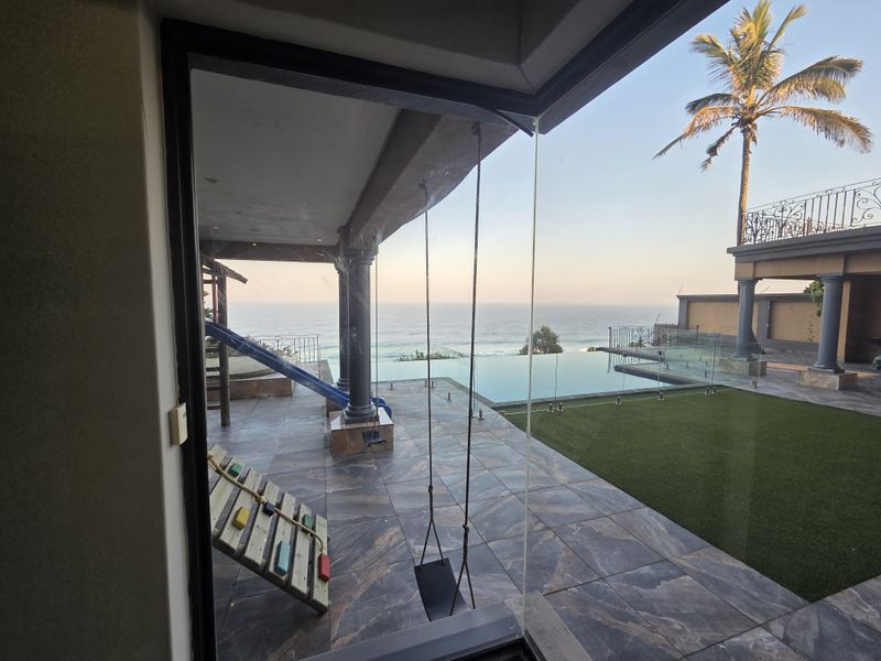 Stunning ocean view from a tiled patio featuring an infinity pool, glass balustrades, and well-maintained outdoor living space.
