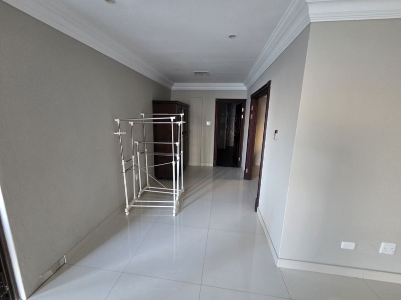 A spacious hallway featuring neutral wall tones, tiled flooring, and decorative cove cornicing, leading to adjacent rooms.