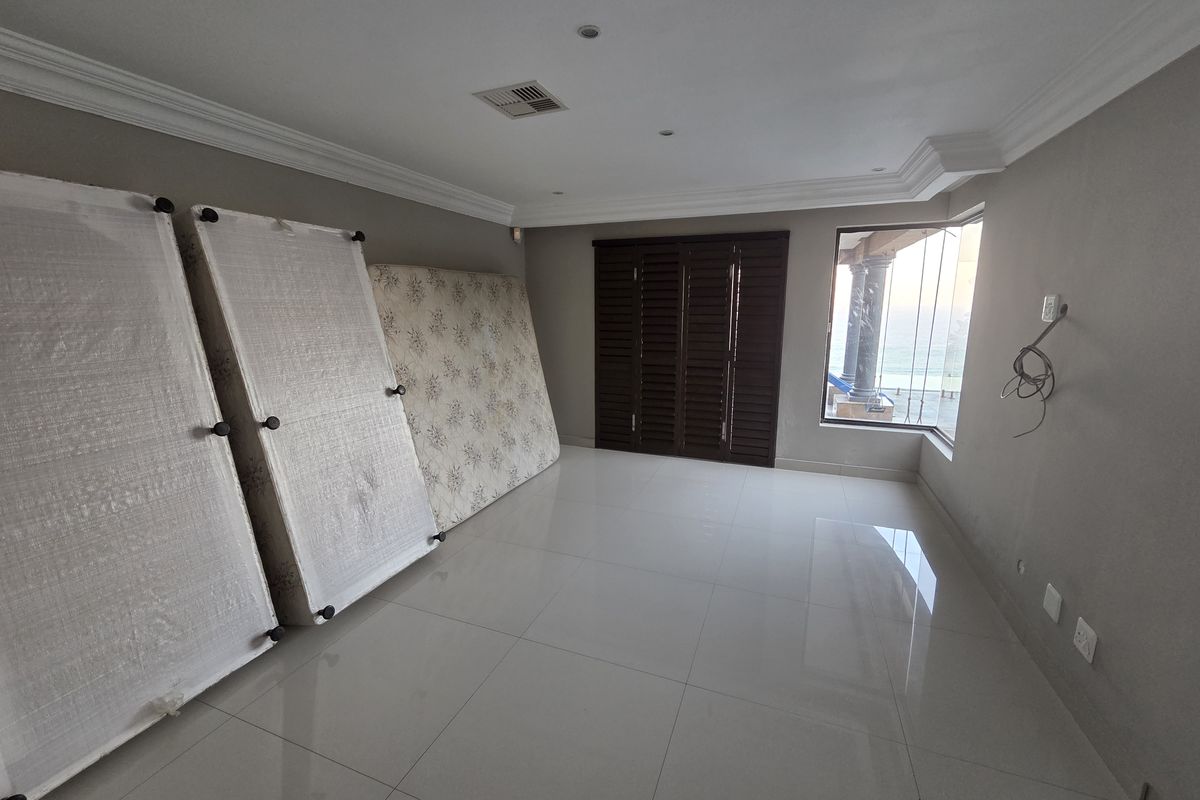 Spacious living area featuring large format floor tiles, crown molding, and wooden shutters, with a bay window providing natural light and exterior views.