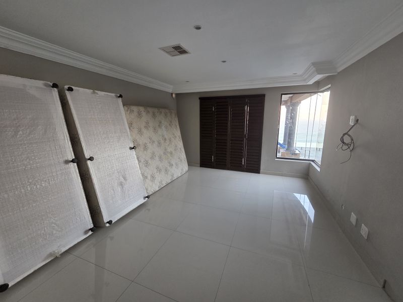 Spacious living area featuring large format floor tiles, crown molding, and wooden shutters, with a bay window providing natural light and exterior views.