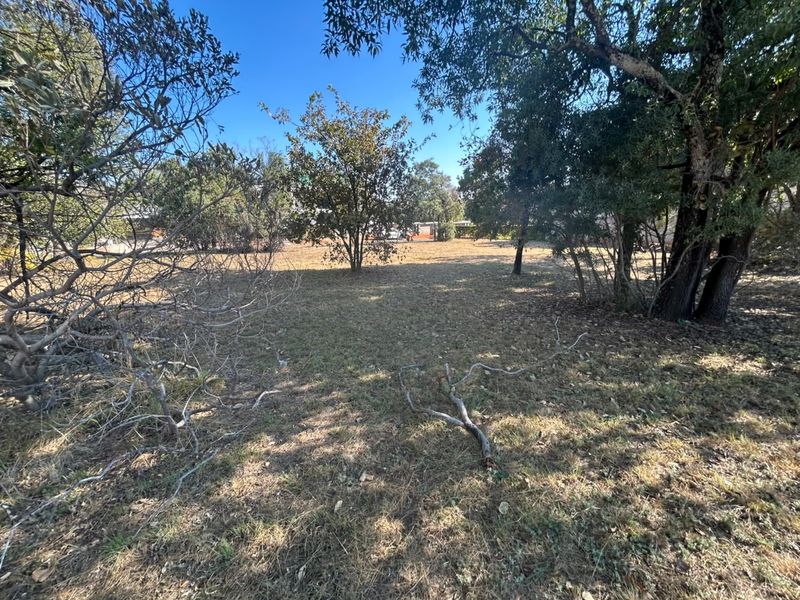 A view of a vacant residential plot featuring established trees and natural grass coverage.