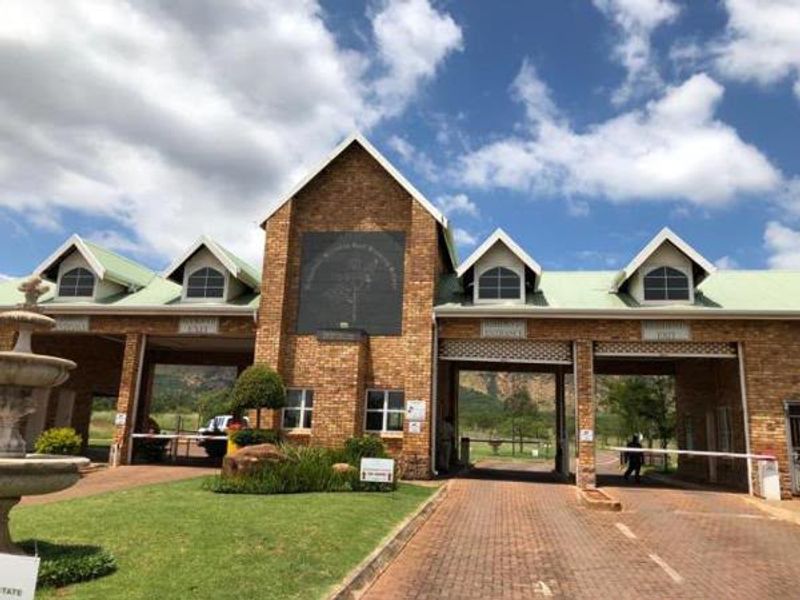 A well-maintained brick security gatehouse entrance for a residential estate, featuring gabled roof architecture, paved access lanes, and landscaped garden surroundings.