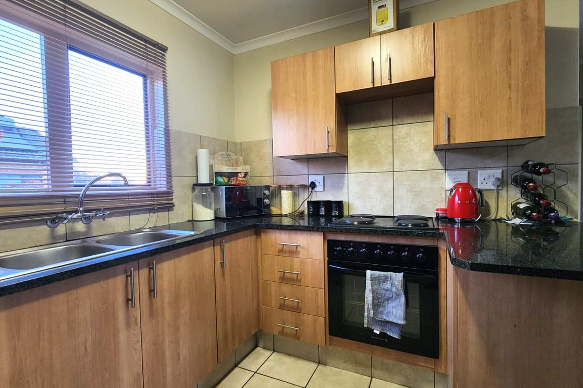 Functional kitchen featuring laminate cabinetry, granite countertops, a double bowl sink, and built-in oven with electric hob.