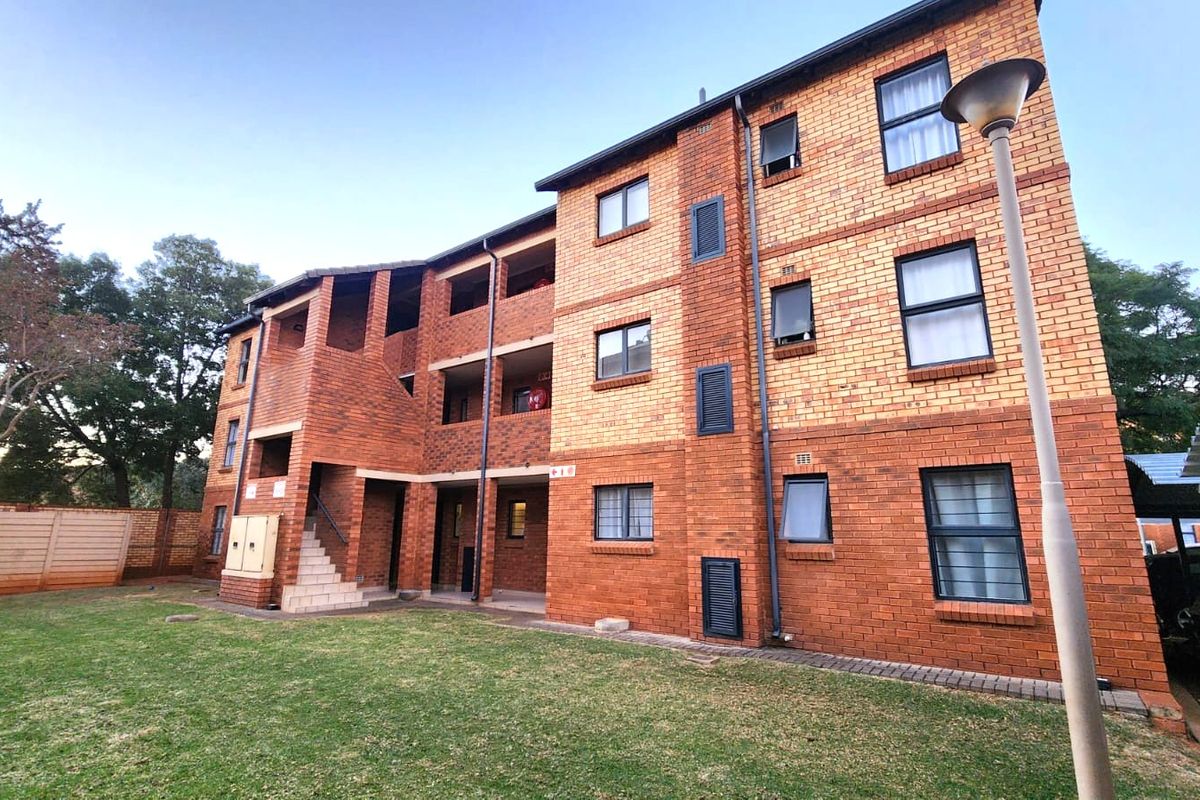 A multi-story apartment building featuring a face-brick exterior, communal staircase, and landscaped garden area with adjacent paved parking.