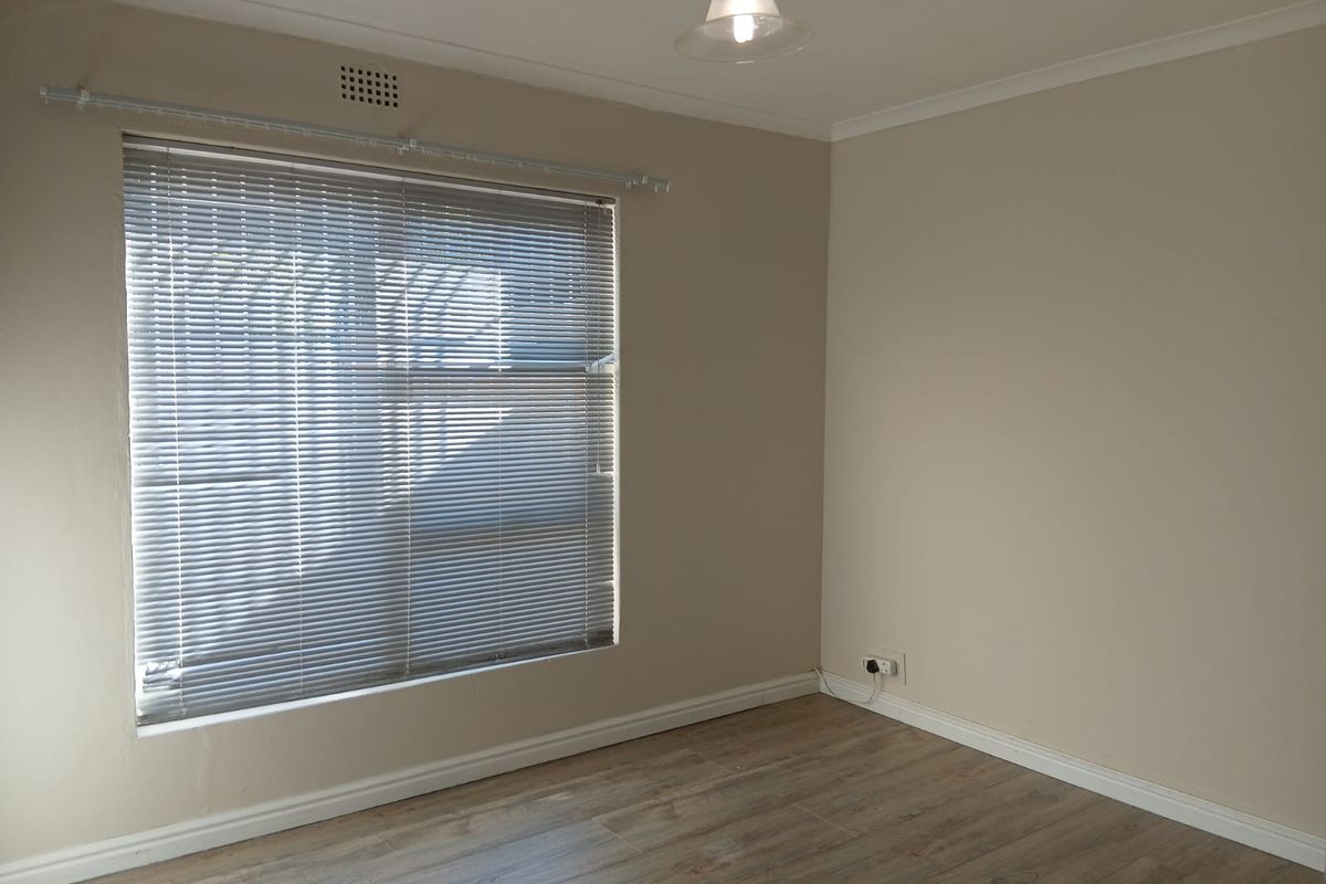 A clean, empty bedroom featuring neutral wall tones, modern laminate flooring, and fitted venetian blinds, offering a versatile space ready for personalization.