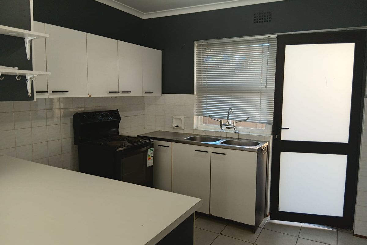 Functional kitchen featuring white cabinetry, tiled backsplash, double sink, and direct access to the exterior via a frosted glass door.