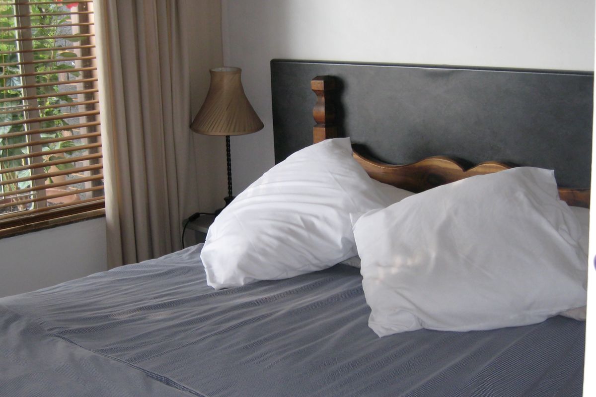 A bedroom featuring a window with venetian blinds, providing natural light and a view of the exterior greenery.