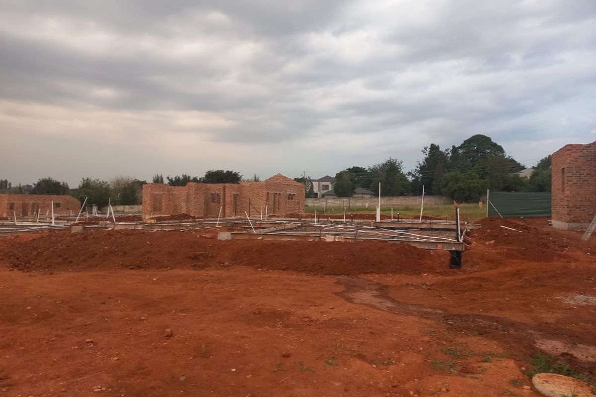 A residential construction site showing brick walls and concrete foundations with plumbing rough-ins, currently in the early stages of development.