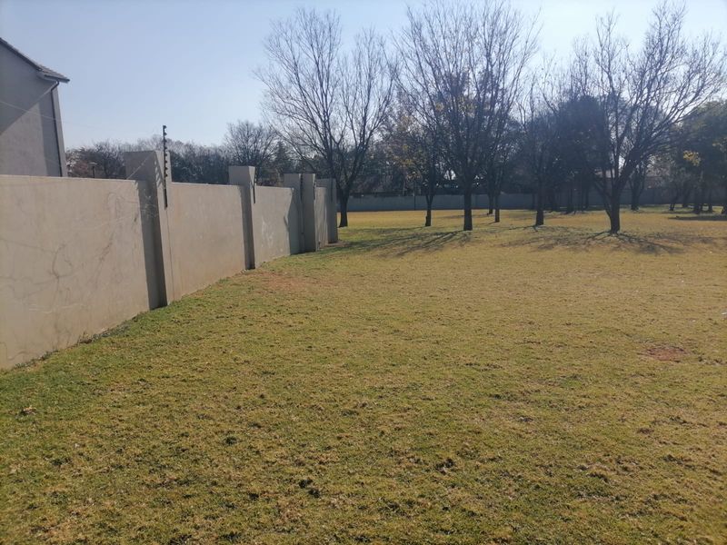 A spacious residential plot featuring a large grassed area, mature trees, and a perimeter wall equipped with electric fencing.