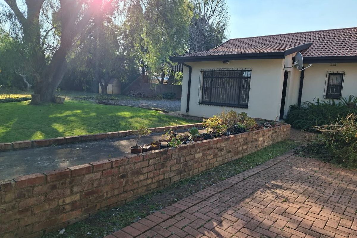 Rear exterior view of the house featuring a brick retaining wall, paved driveway, and a well-maintained garden area.