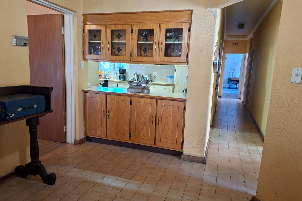 A dated kitchen area featuring traditional wooden cabinetry and tiled flooring, with a convenient pass-through window connecting to the adjacent space.