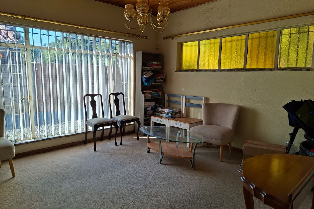 A living room featuring timber ceilings, carpeted flooring, and large windows with security bars, offering a dated aesthetic ready for modernization.