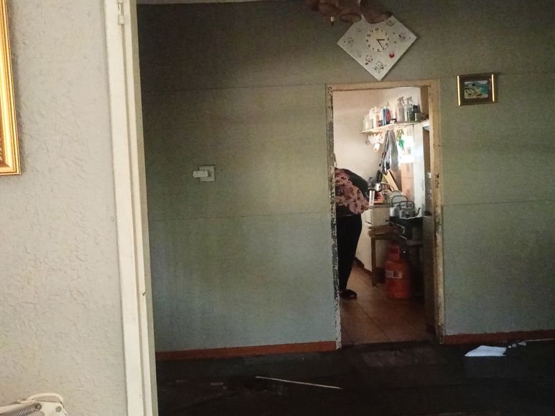 A view from a living area looking into a kitchen space, showing dated wall finishes and worn flooring throughout the interior.