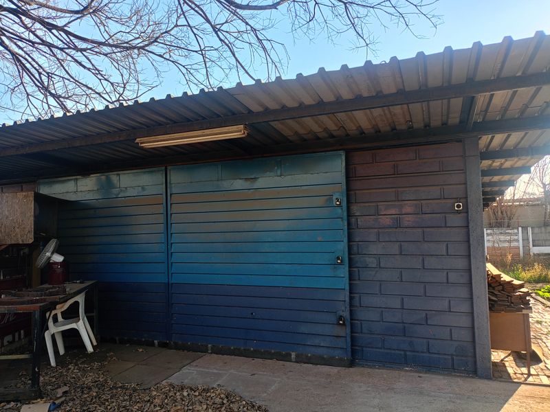 A detached garage structure featuring sliding metal doors, a corrugated roof, and exposed brickwork, showing signs of age and weathering.