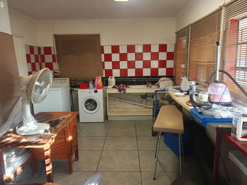A functional laundry room featuring tiled flooring, a built-in utility sink, and a red and white tiled splashback.
