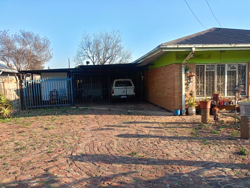 Front exterior view of the house featuring a brick driveway, attached carport with security gate, and brick facade with security bars on windows.