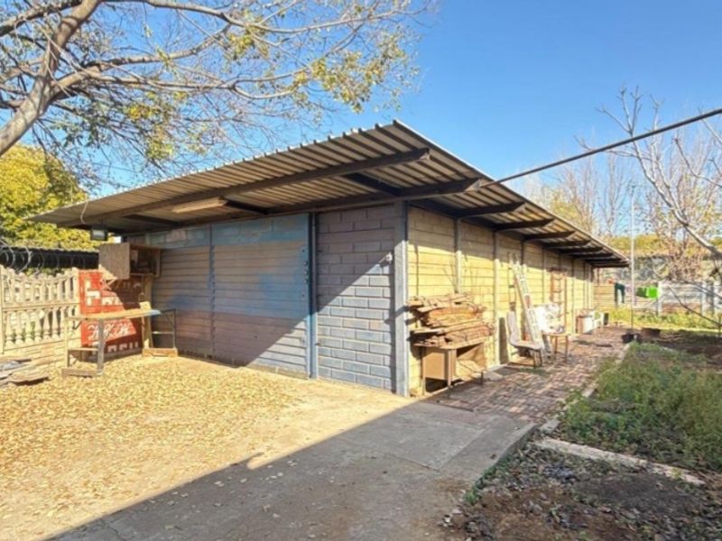 A detached garage structure featuring corrugated metal roofing and concrete block walls, situated in a garden setting with a paved walkway.