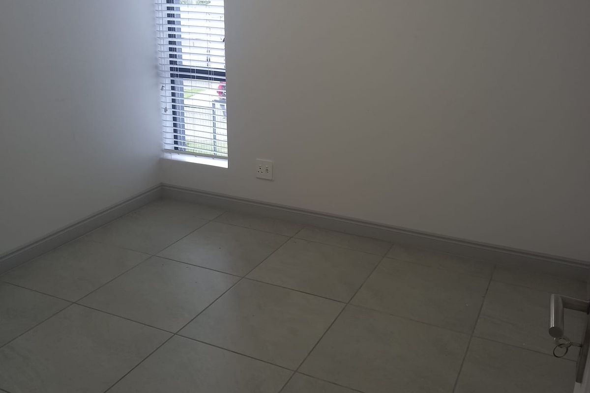 A clean, empty bedroom featuring neutral tiled flooring, white walls, and a tall window with fitted blinds.