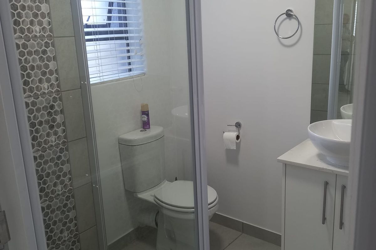 Modern bathroom featuring a glass-enclosed shower with mosaic tile accents, a white vanity with a vessel sink, and neutral floor tiling.