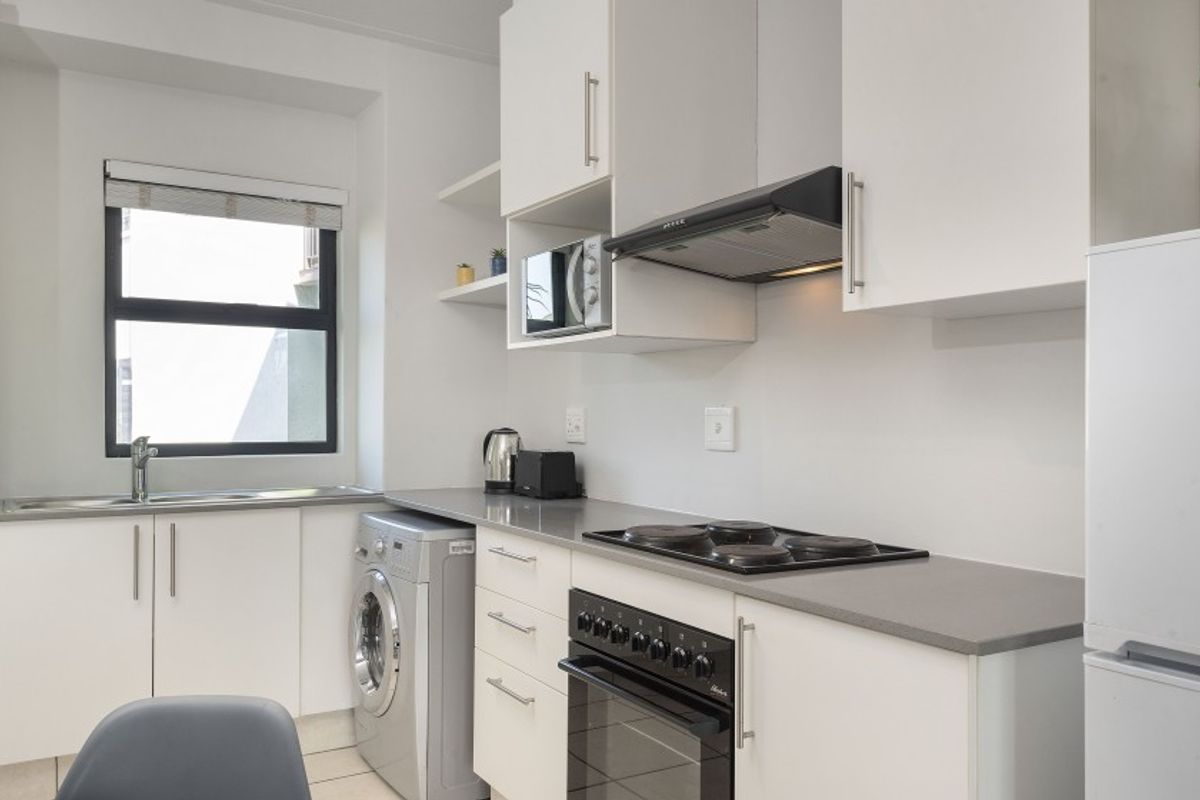 Modern kitchen featuring white cabinetry, stone countertops, integrated electric hob, oven, extractor fan, and a stainless steel sink with a window view.