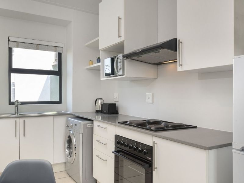 Modern kitchen featuring white cabinetry, stone countertops, integrated electric hob, oven, extractor fan, and a stainless steel sink with a window view.