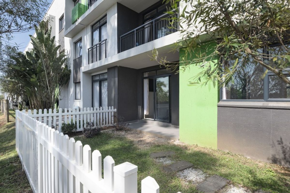 Ground floor apartment exterior featuring a private patio, small garden area, and white picket fence with modern building facade.