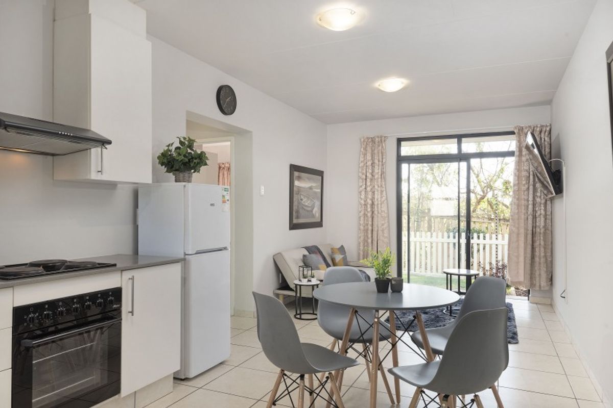 An open-plan living and kitchen area featuring tiled floors, modern cabinetry, built-in cooking appliances, and sliding glass doors leading to an outdoor space.