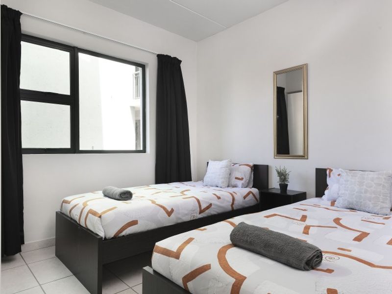 A well-lit bedroom featuring tiled flooring and a large aluminium-framed window, providing a clean and functional living space.