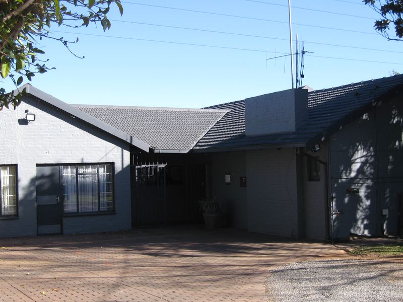 Front elevation of a single-story brick house featuring a paved driveway, tiled roof, and secure gated entrance.