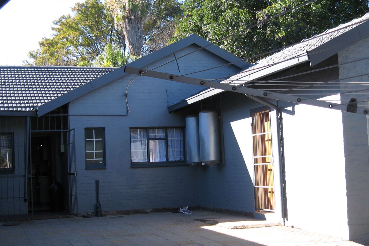 Rear exterior view of the property featuring a paved courtyard, security gates, and external geysers mounted on the brick wall.