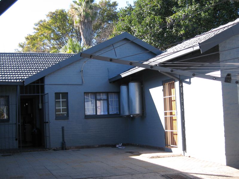 Rear exterior view of the property featuring a paved courtyard, security gates, and external geysers mounted on the brick wall.