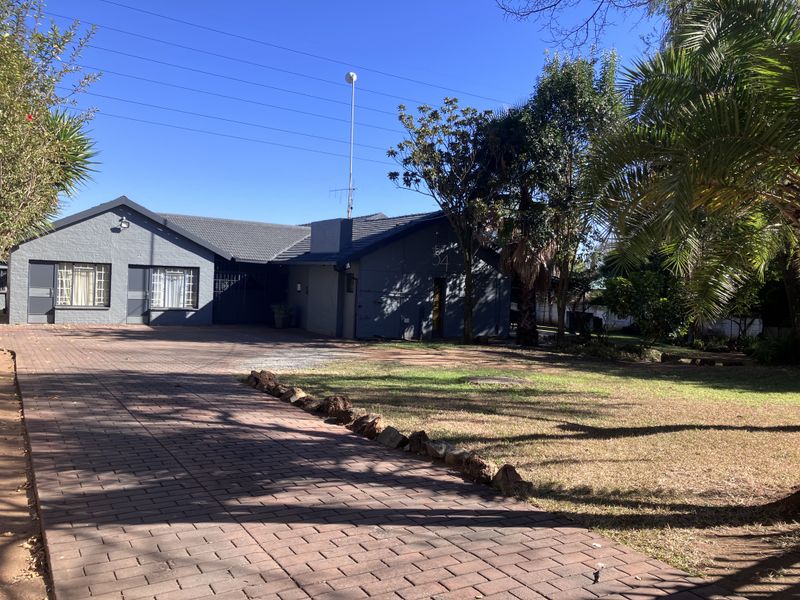 Front exterior view of a single-story brick house featuring a paved driveway, tiled roof, and established garden area.