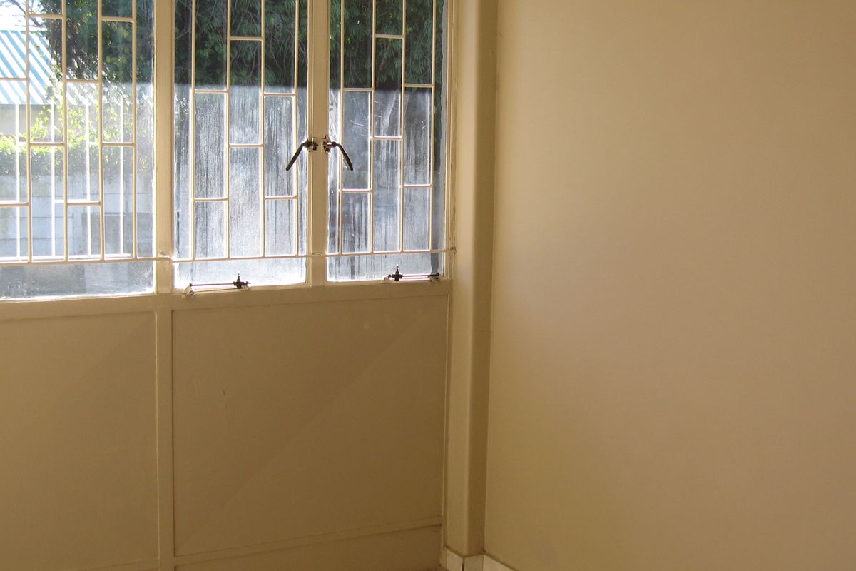An empty room featuring tiled flooring and large windows fitted with security bars, offering a neutral canvas for potential interior design updates.