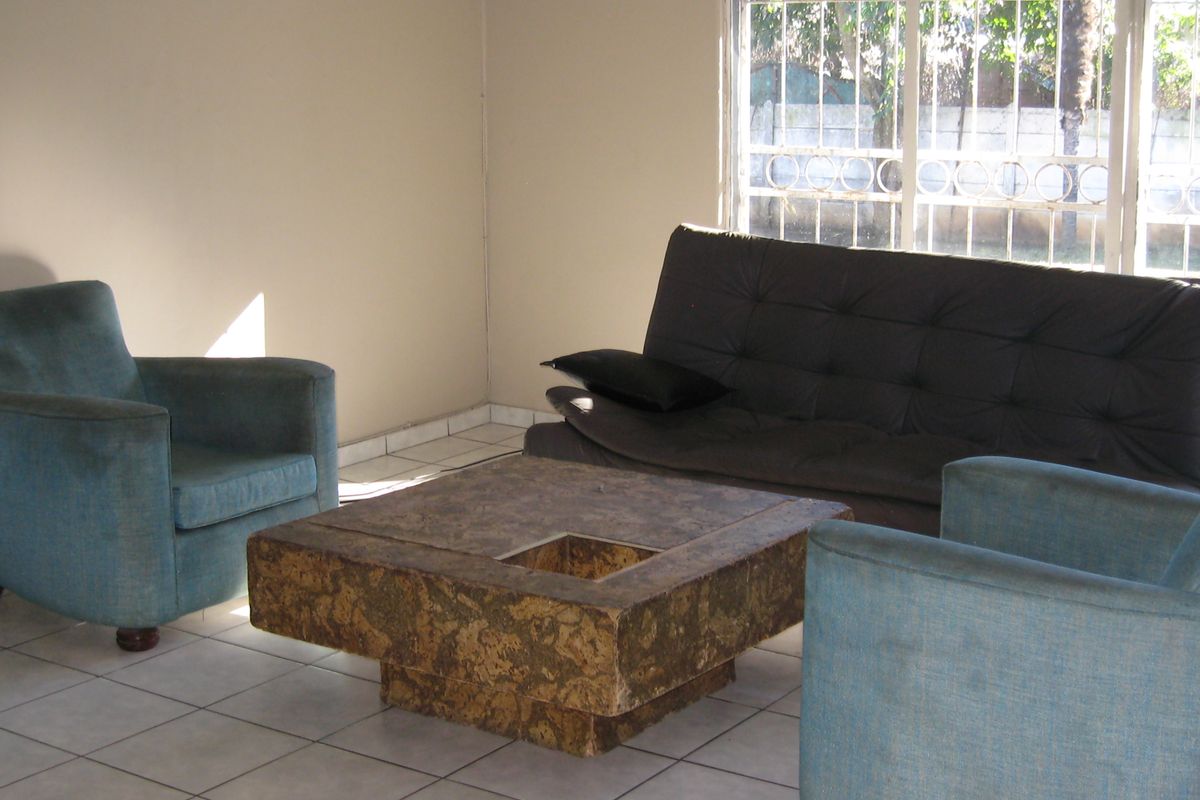 A living room area featuring tiled flooring and a large window with security bars, offering a blank canvas for potential interior updates.
