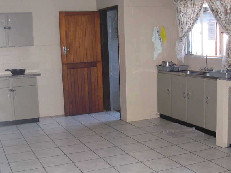 A functional kitchen featuring tiled flooring, built-in cabinetry, laminate countertops, and a stainless steel sink with a tiled splashback.