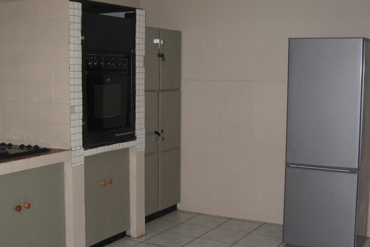A functional kitchen featuring built-in cabinetry, a wall-mounted oven, and a gas hob with tiled splashbacks and flooring.