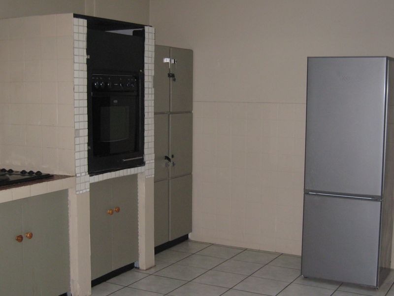 A functional kitchen featuring built-in cabinetry, a wall-mounted oven, and a gas hob with tiled splashbacks and flooring.