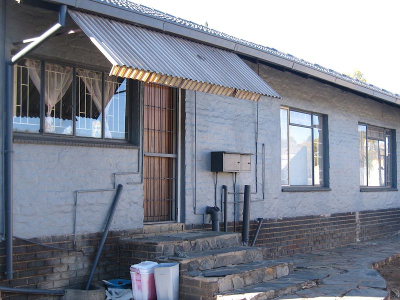 Front elevation of a single-story house featuring a corrugated metal awning, security gates, and stone steps leading to the entrance.