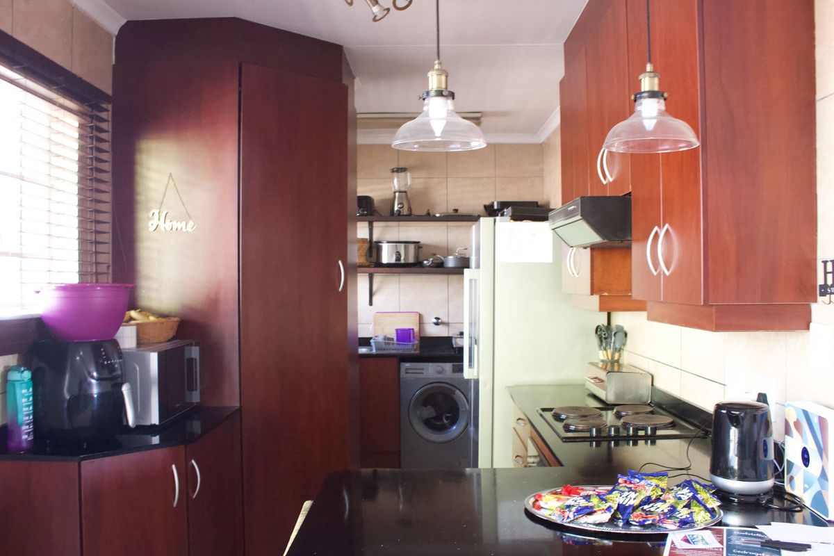 A functional kitchen featuring dark wood cabinetry, black granite countertops, an electric hob, and integrated laundry facilities with tiled backsplash and pendant lighting.