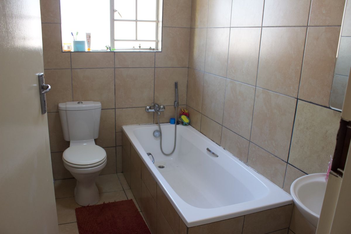 A functional bathroom featuring a bathtub with a handheld shower attachment, a standard toilet, and neutral wall and floor tiling.