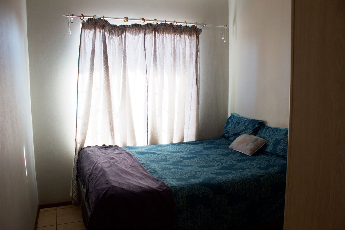 A compact bedroom featuring tiled flooring, a built-in wardrobe, and a window dressed with a curtain rod.