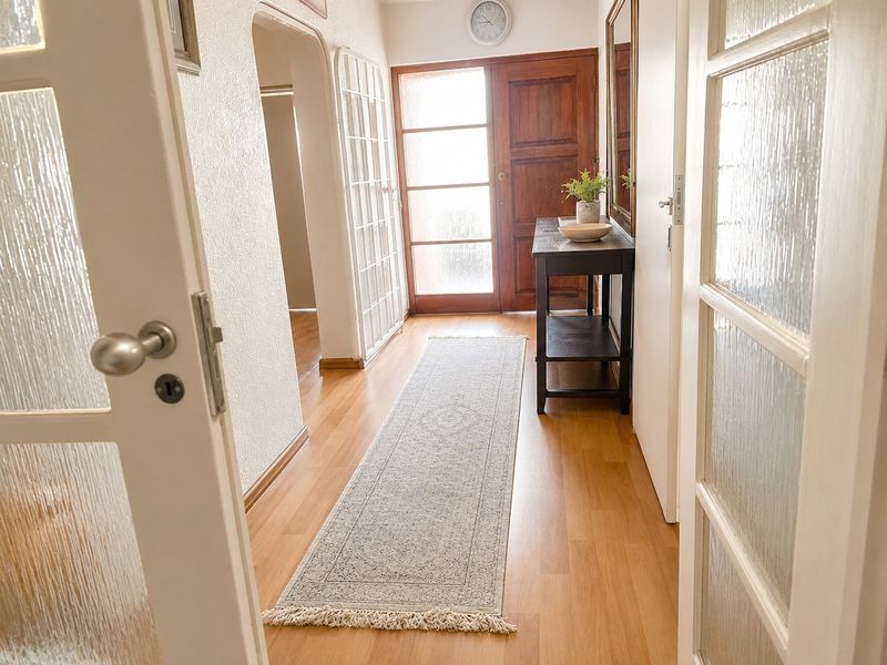 A bright, welcoming hallway featuring timber front door, laminate flooring, and classic archway detailing leading into the home.