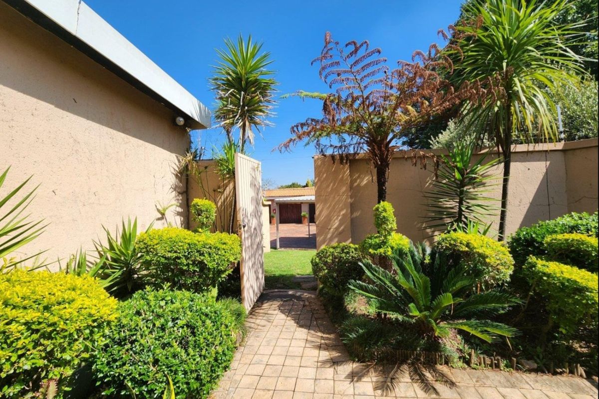 A rear garden area featuring a paved walkway leading through a gate, surrounded by established boundary walls and landscaped garden beds.