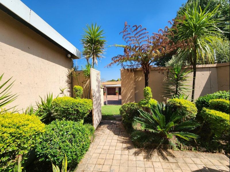 A rear garden area featuring a paved walkway leading through a gate, surrounded by established boundary walls and landscaped garden beds.